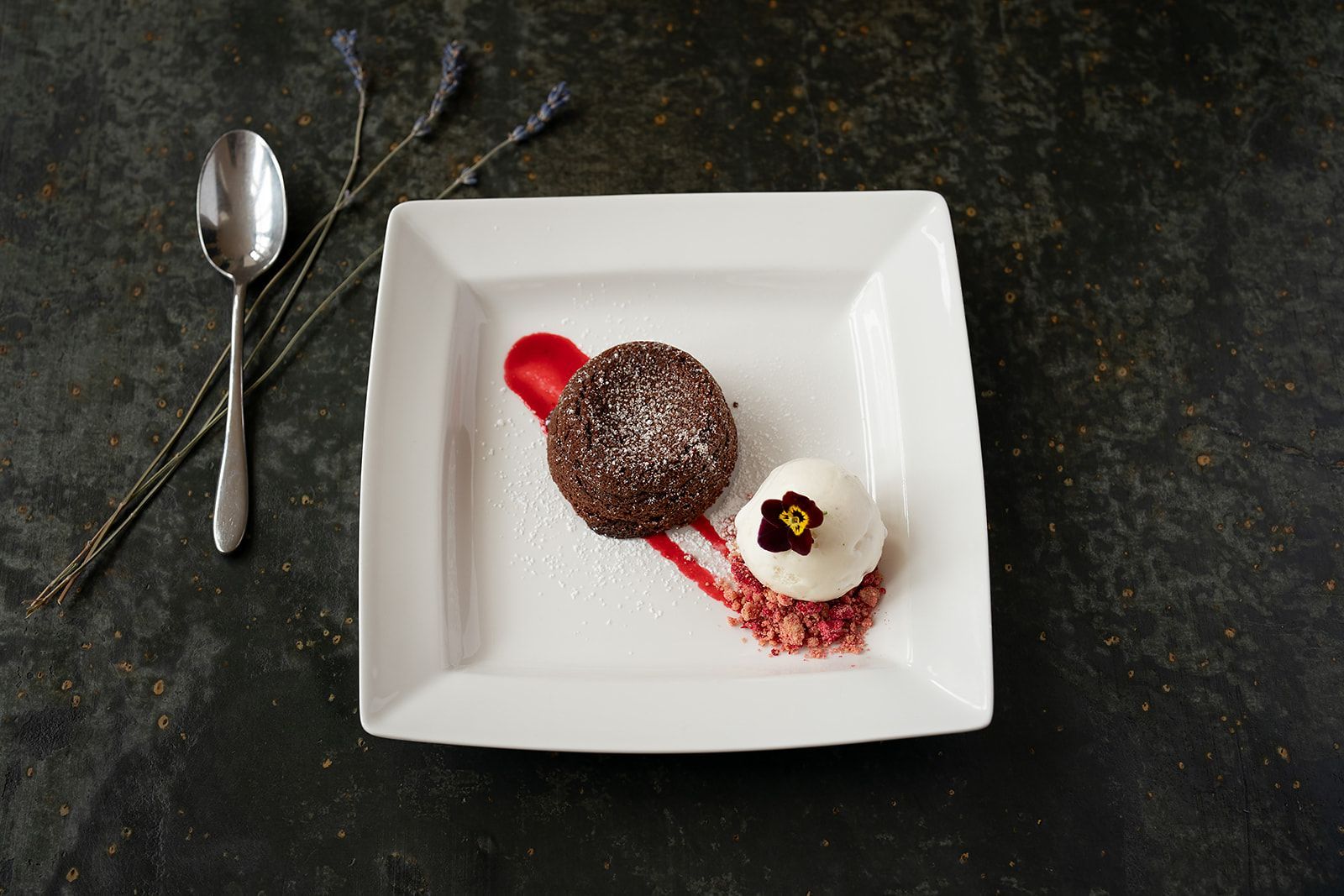 A white plate topped with a chocolate cake and ice cream next to a spoon.