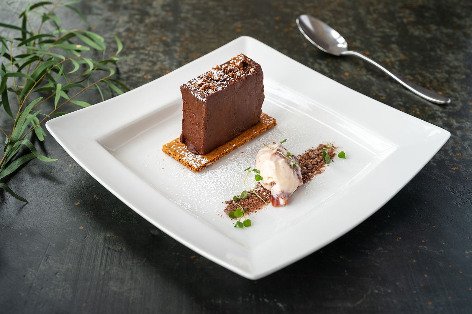 A white plate topped with a piece of chocolate cake and ice cream next to a spoon.