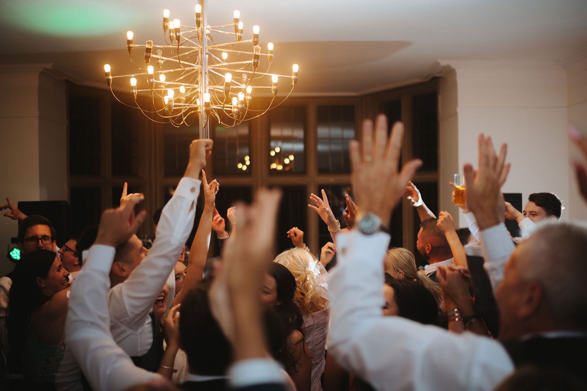 A crowd of people are dancing in a room with their hands in the air.