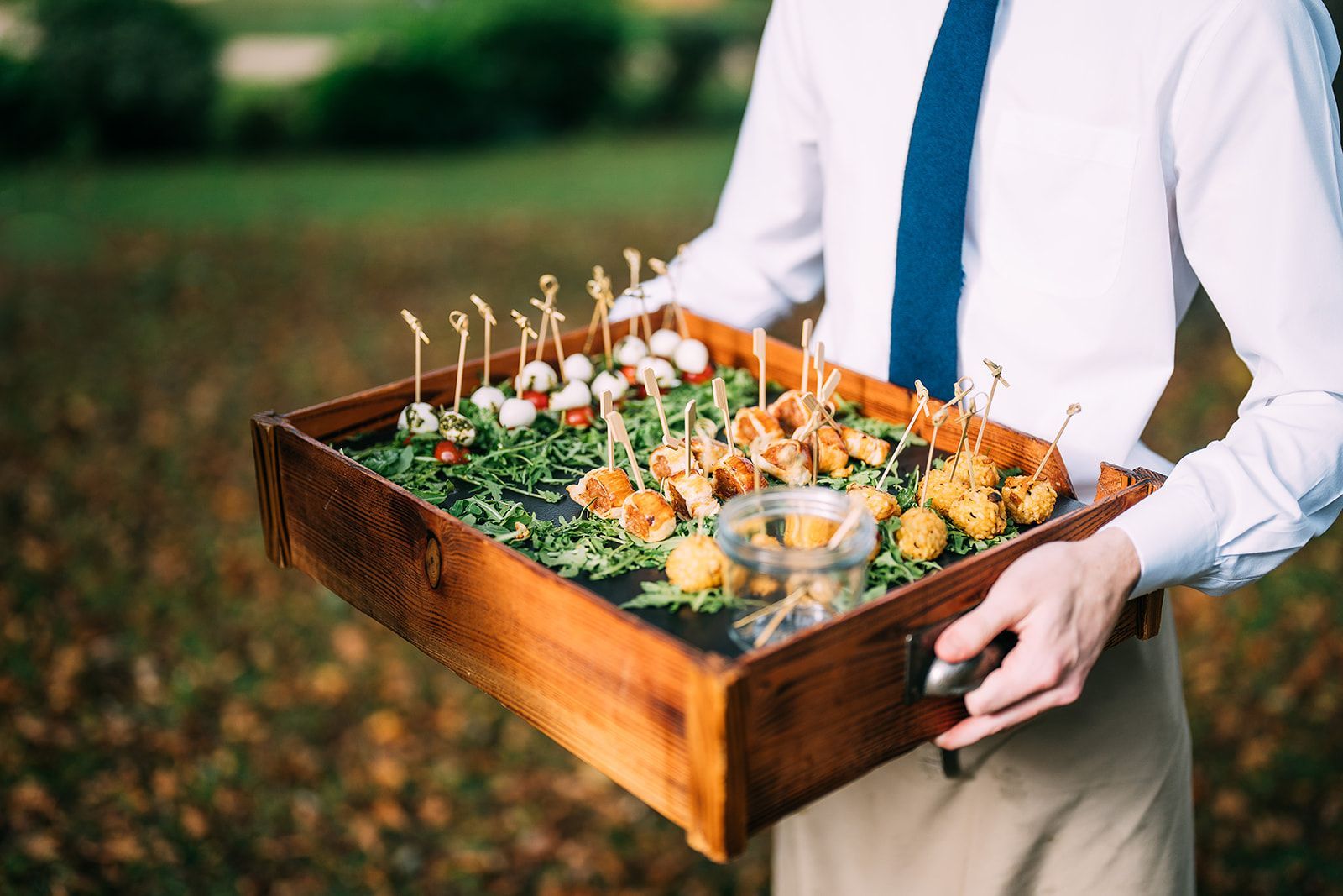 A man in a tie is holding a wooden tray of food.