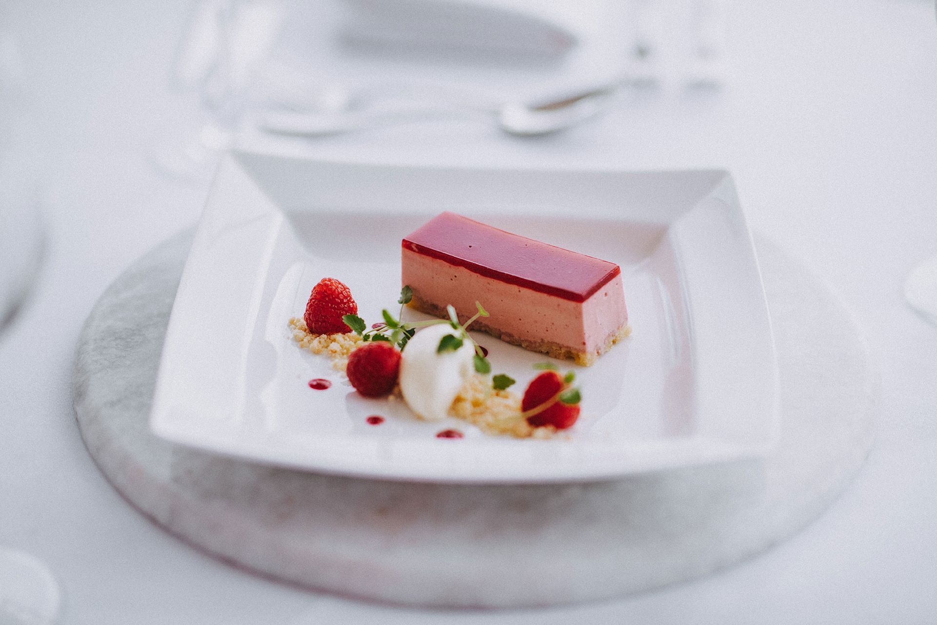 A dessert with raspberries and whipped cream on a white plate on a table.