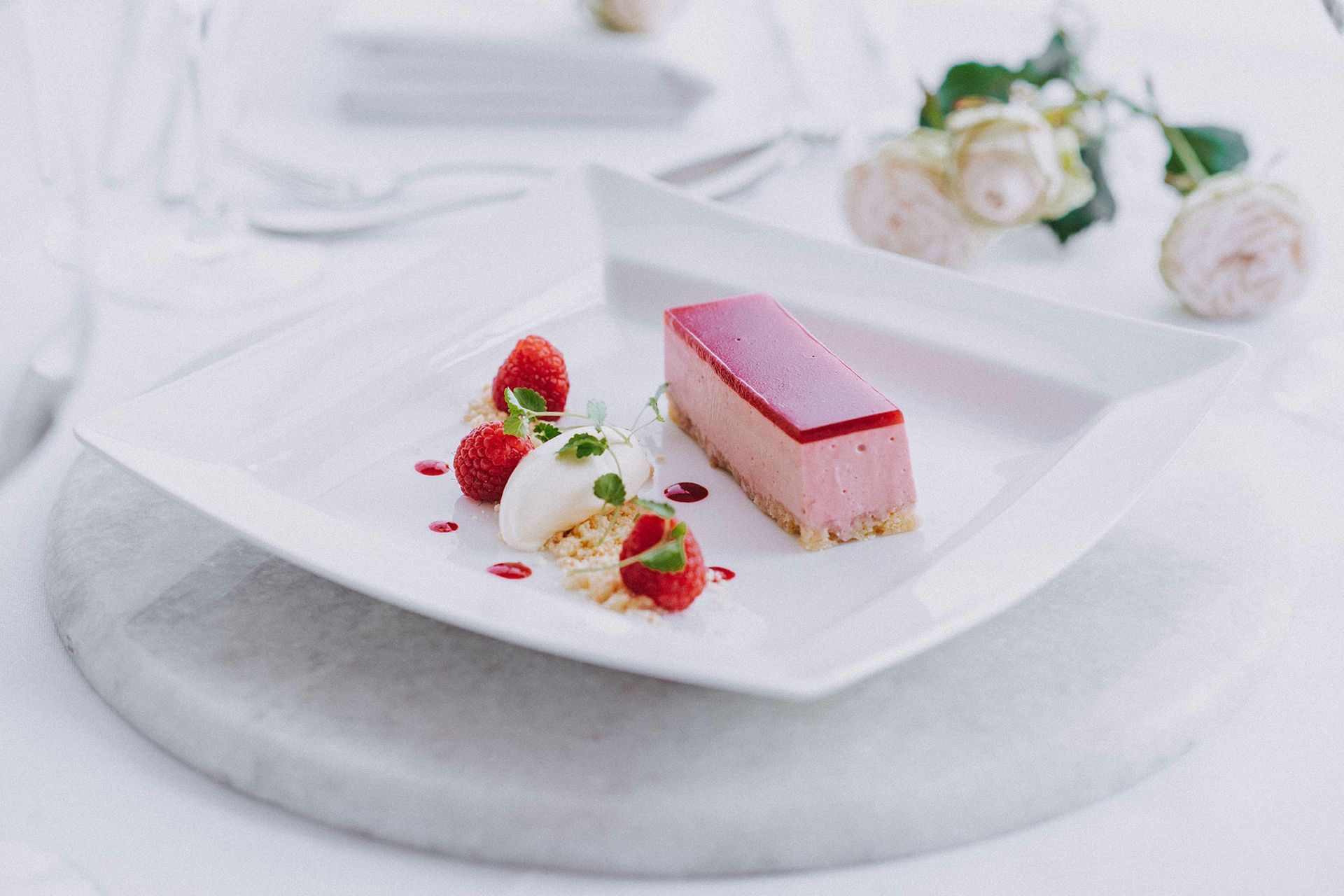 A white plate topped with a pink dessert and raspberries on a table.