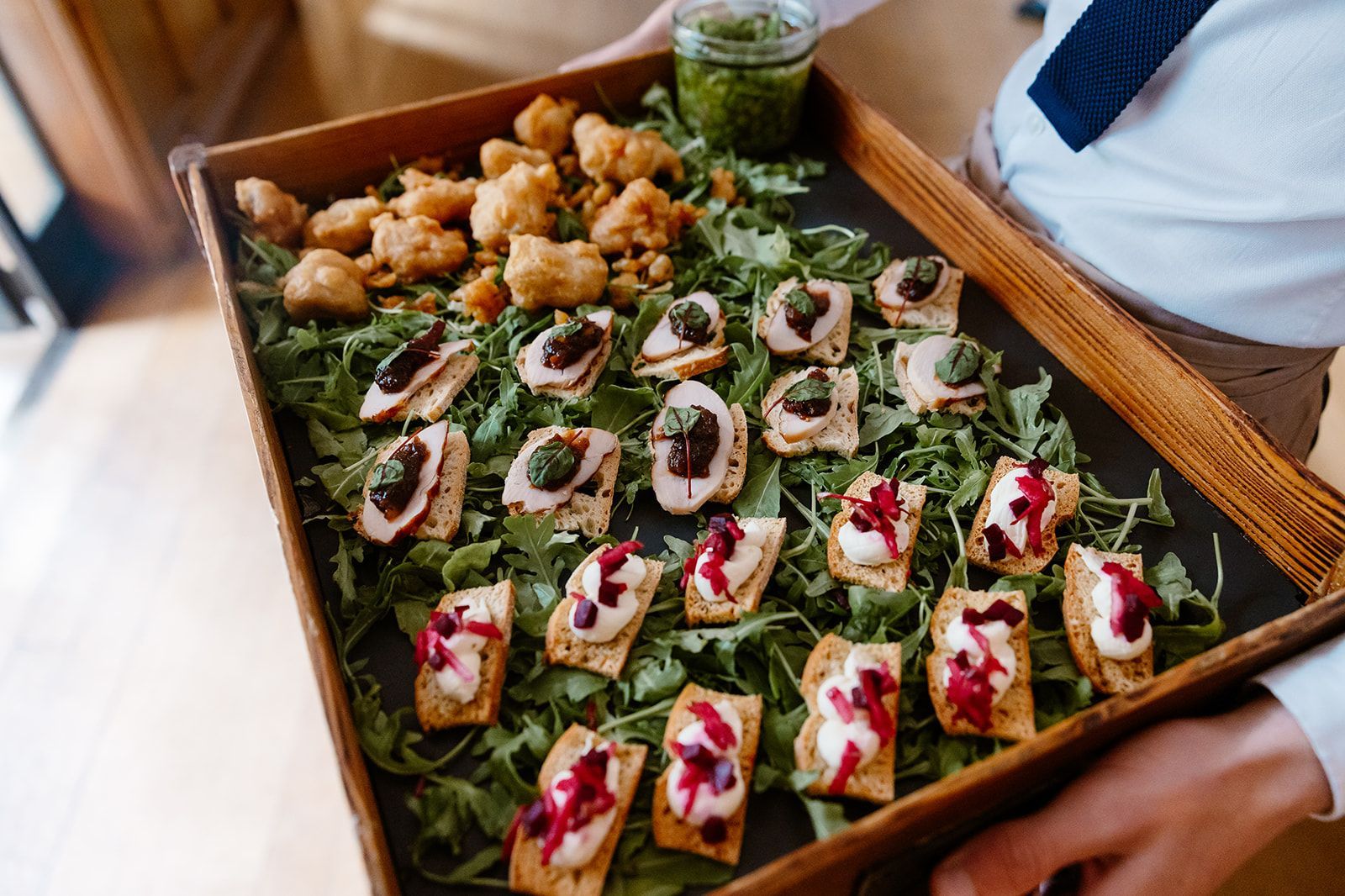 A person is holding a wooden tray of food.
