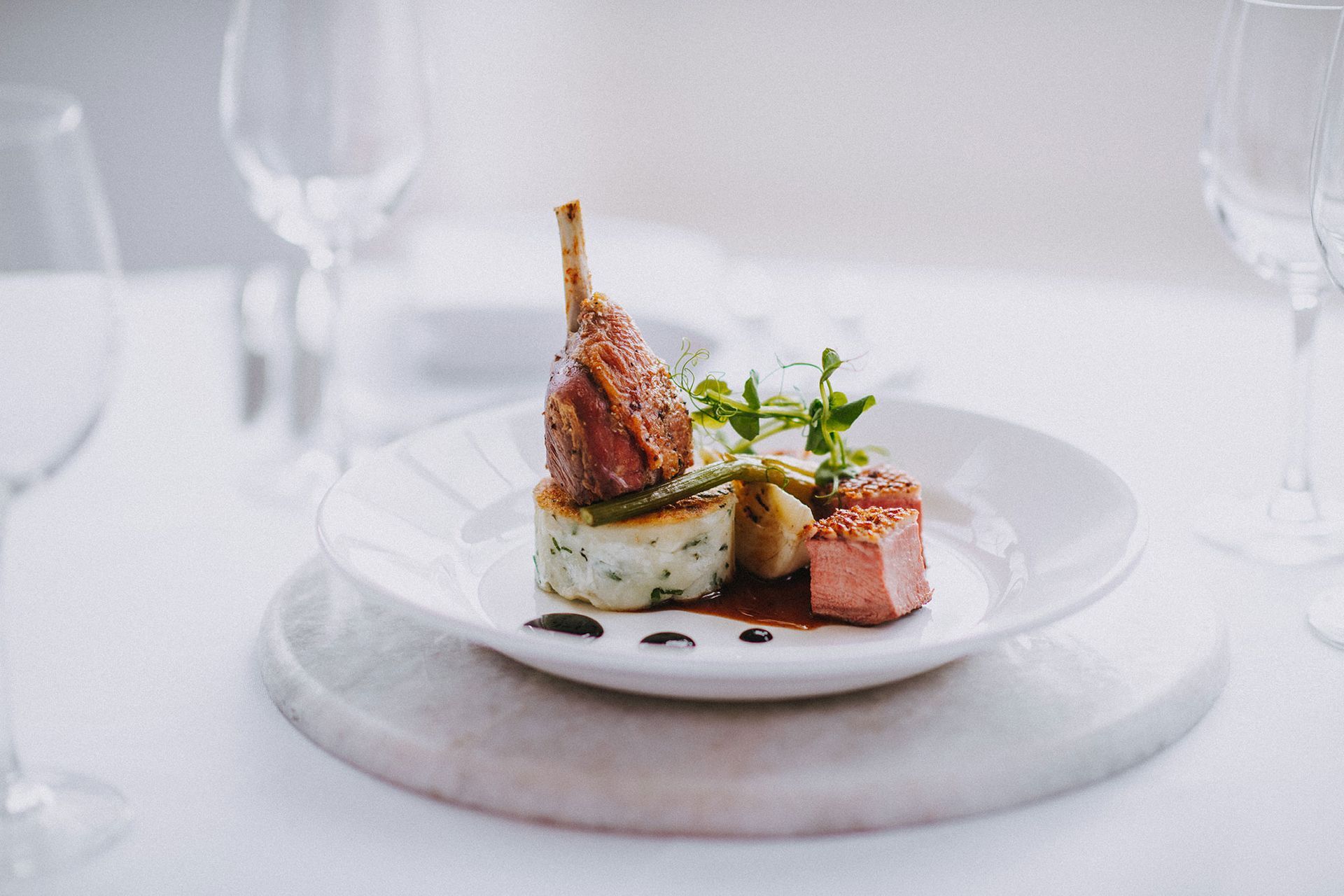 A close up of a plate of food on a table with wine glasses.