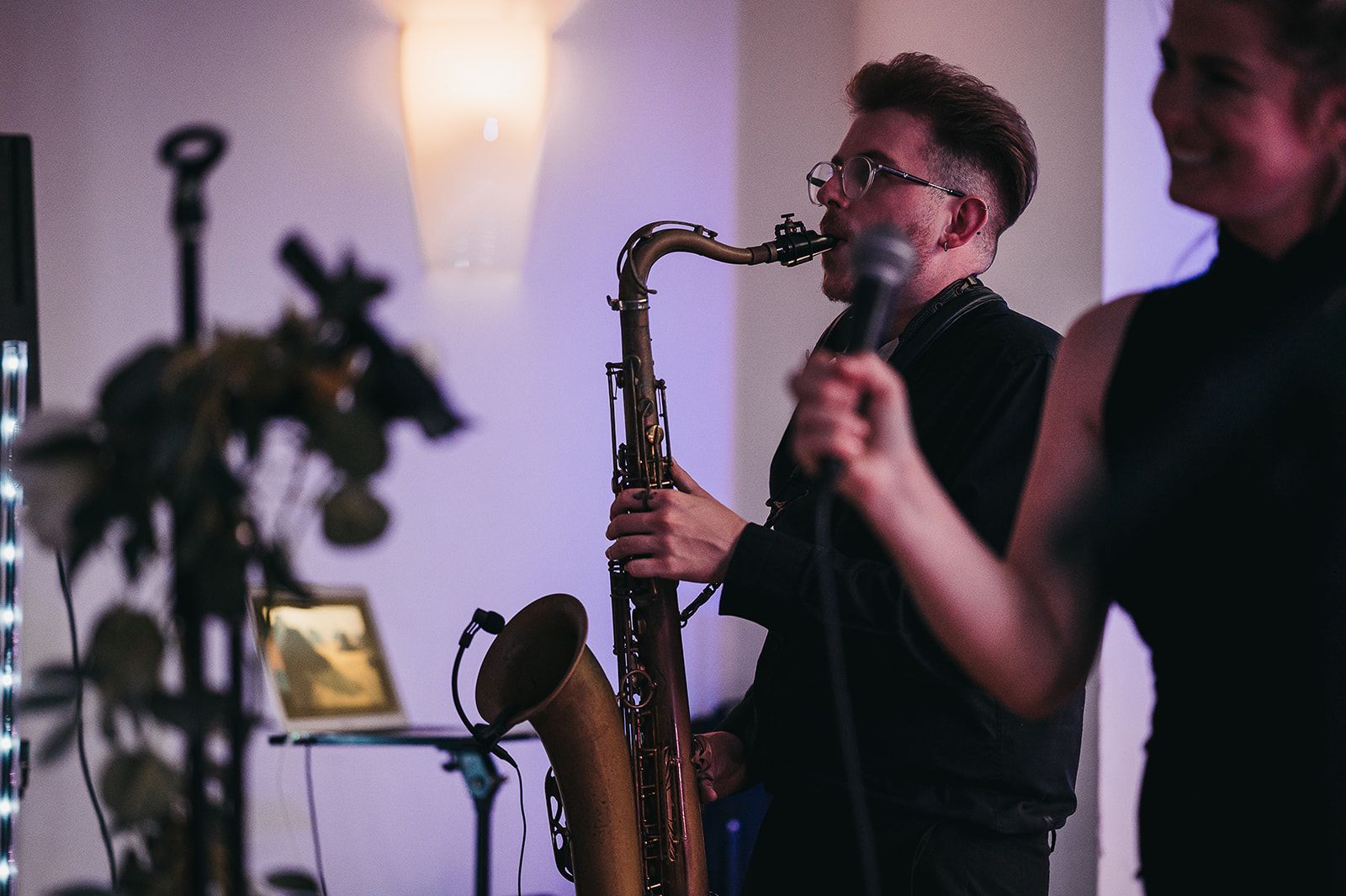 A man is playing a saxophone and a woman is singing into a microphone.