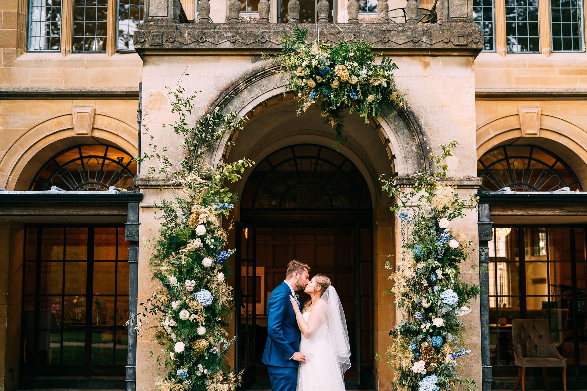 A bride and groom are kissing in front of a building decorated with flowers.