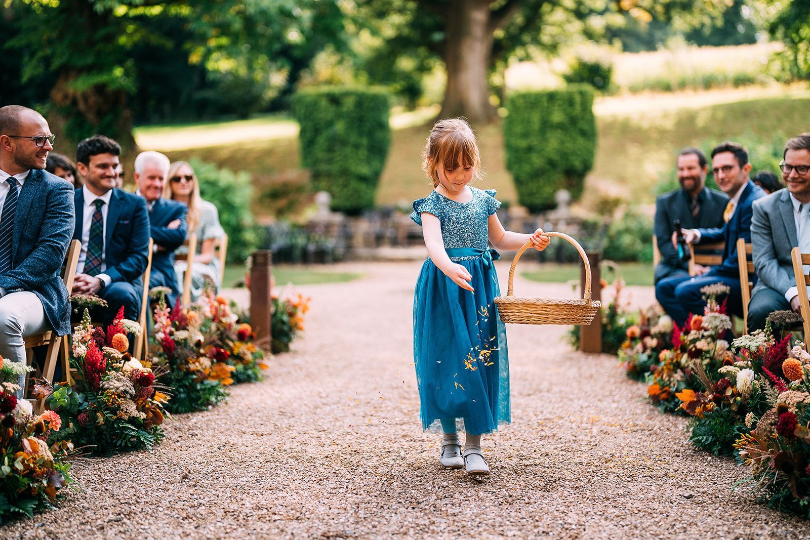 A flower girl is walking down the aisle at a wedding holding a basket of flowers.