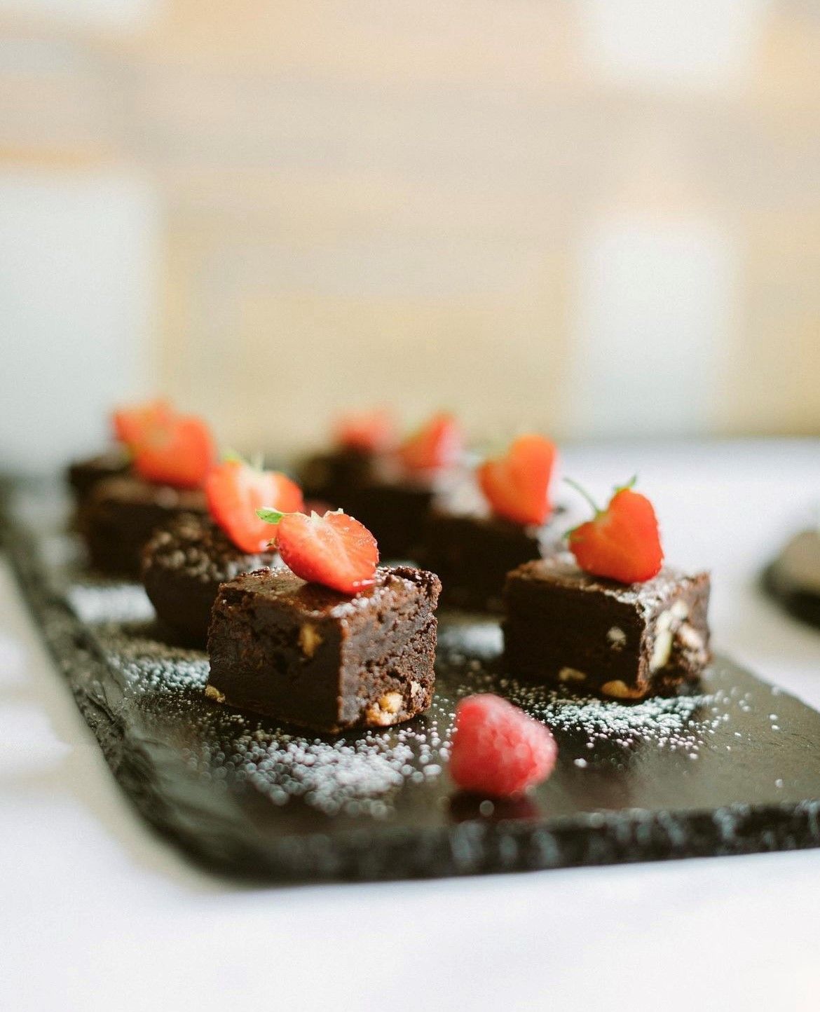 A tray of brownies with strawberries on top on a table.