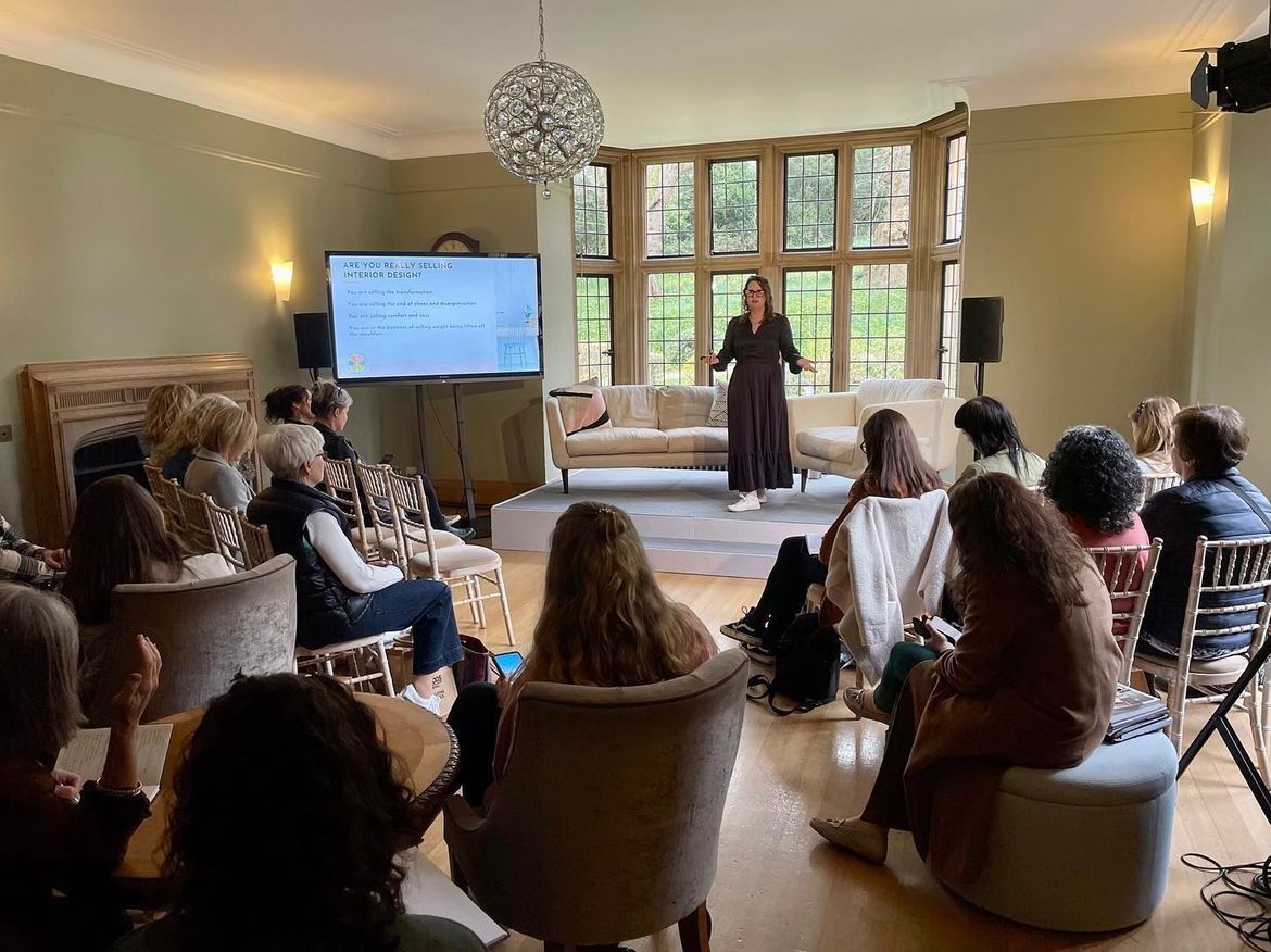 A woman is giving a presentation to a group of people in a living room.