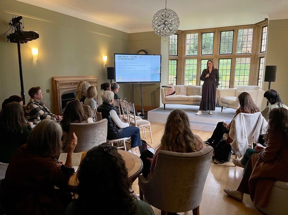A woman is giving a presentation to a group of people in a living room.