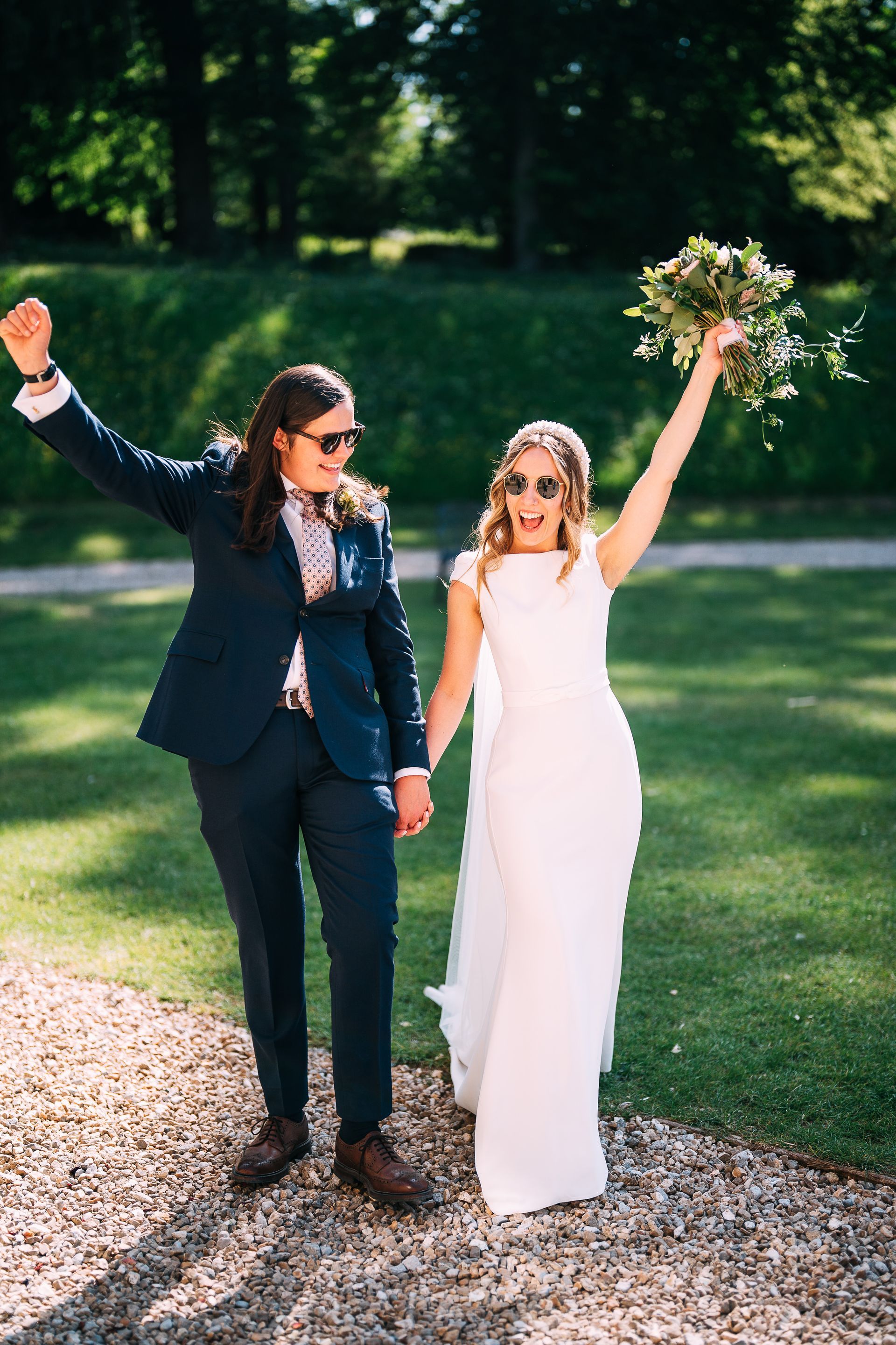A bride and groom are holding hands and raising their arms in the air.