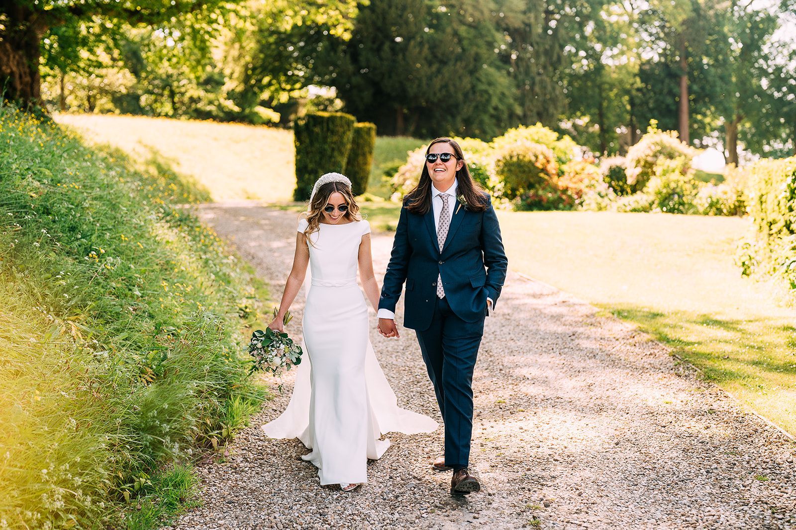 A bride and groom are walking down a gravel road holding hands.