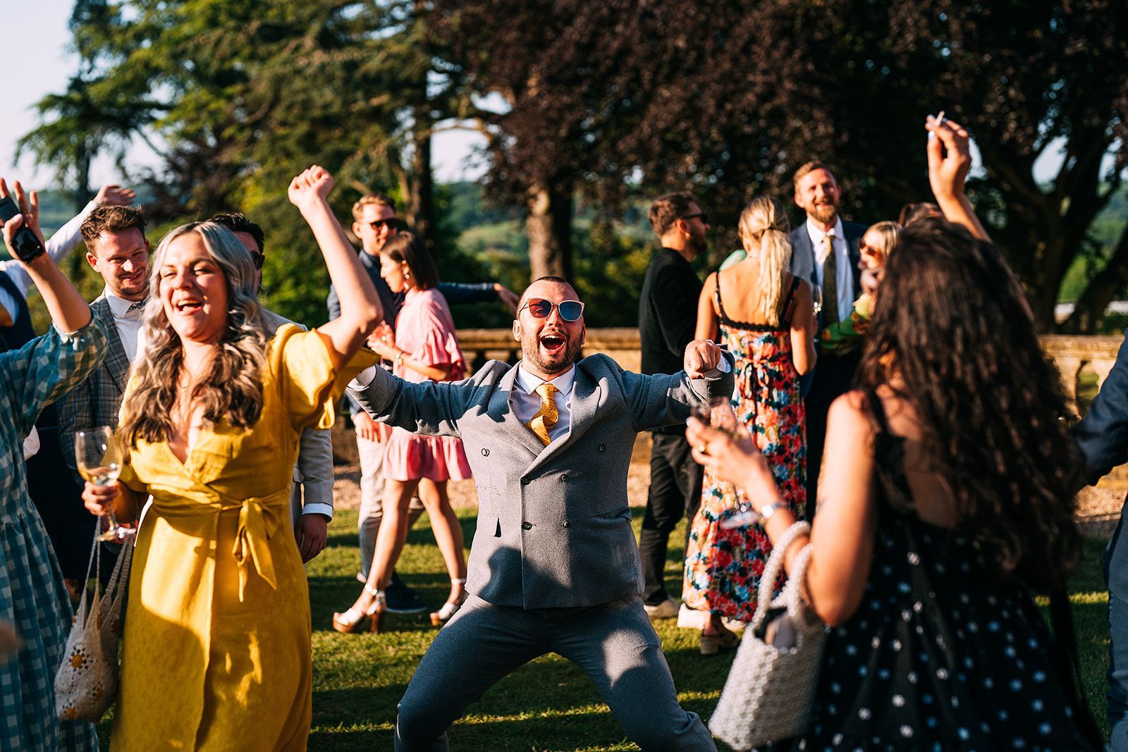A group of people are dancing in a field at a wedding reception.