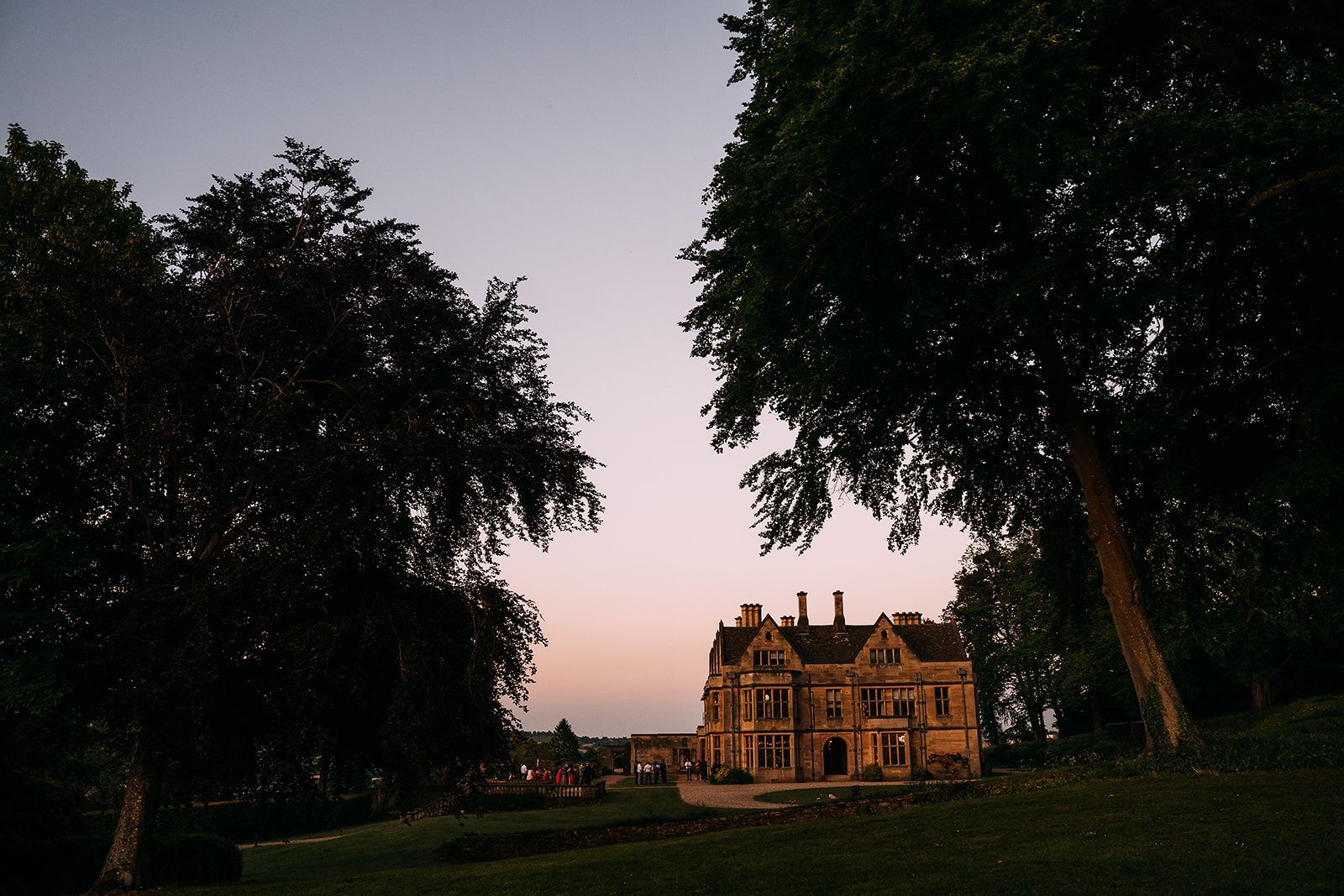 A large house sits in the middle of a field surrounded by trees
