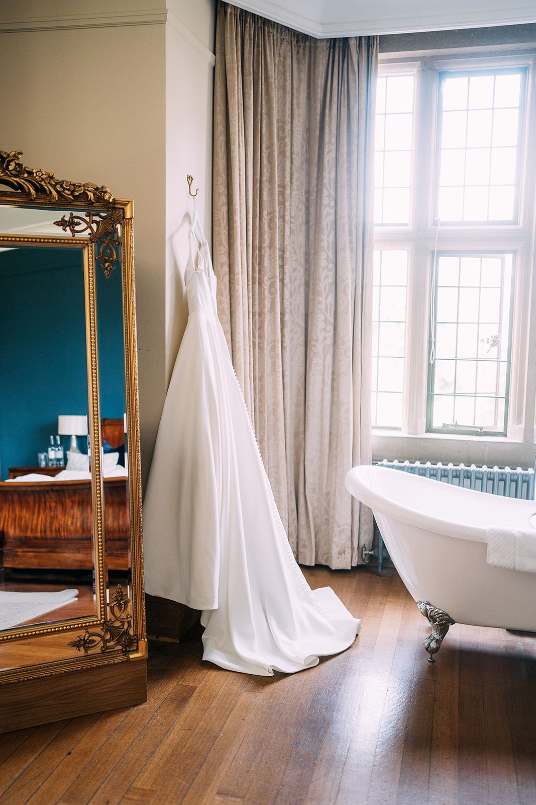 A wedding dress is hanging on a hanger in a bathroom next to a bathtub.