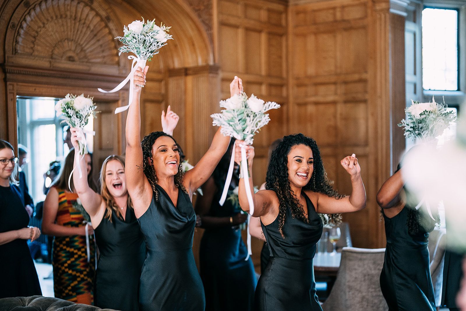 A group of bridesmaids are holding their bouquets in the air.