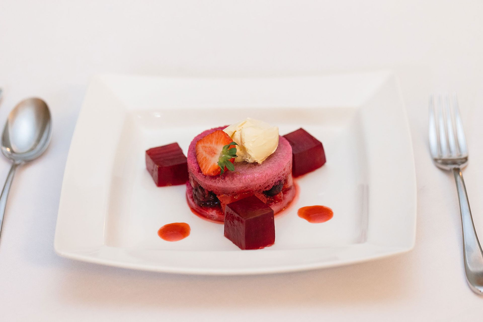A white plate topped with a dessert next to a fork and spoon.
