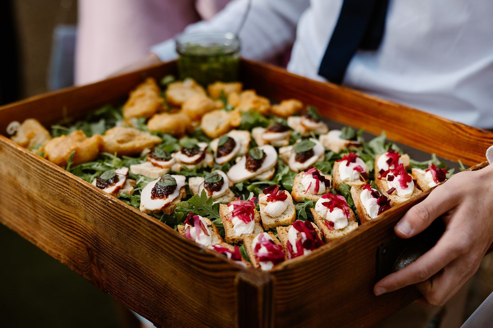 A person is holding a wooden tray filled with appetizers.