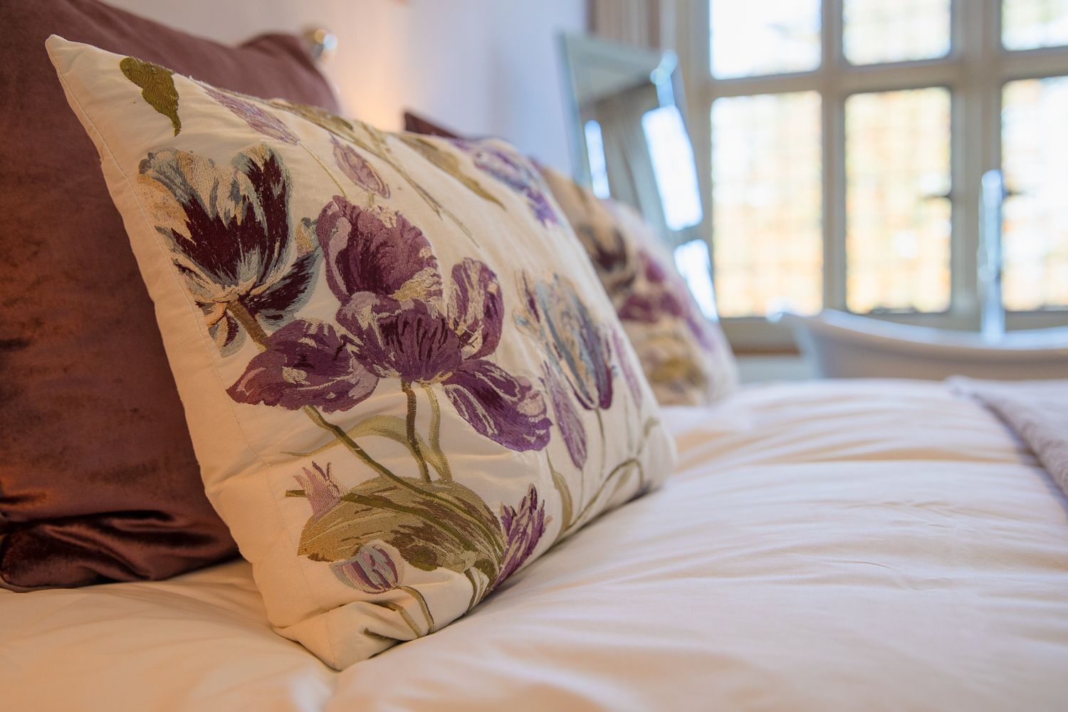 A bed with purple and white pillows and a window in the background.