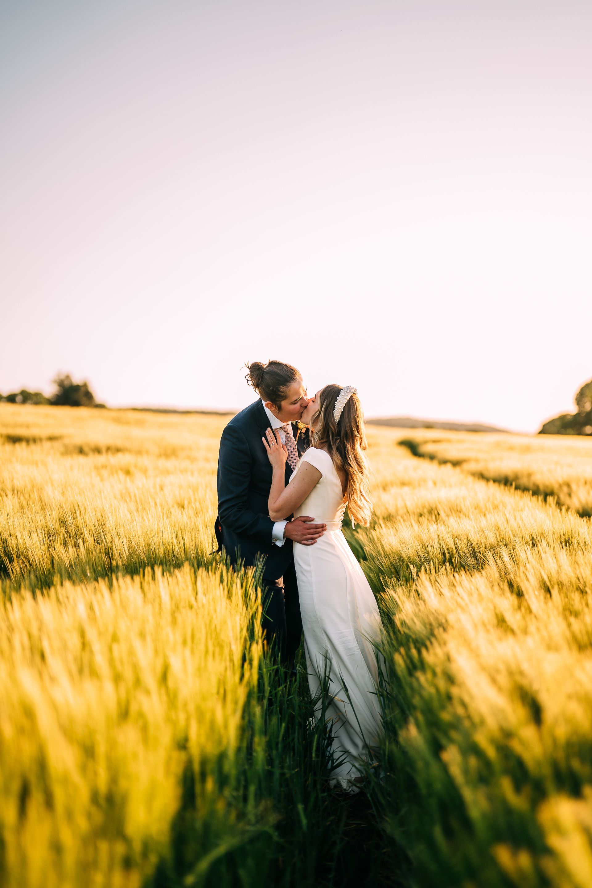 A bride and groom are kissing in a field of wheat.