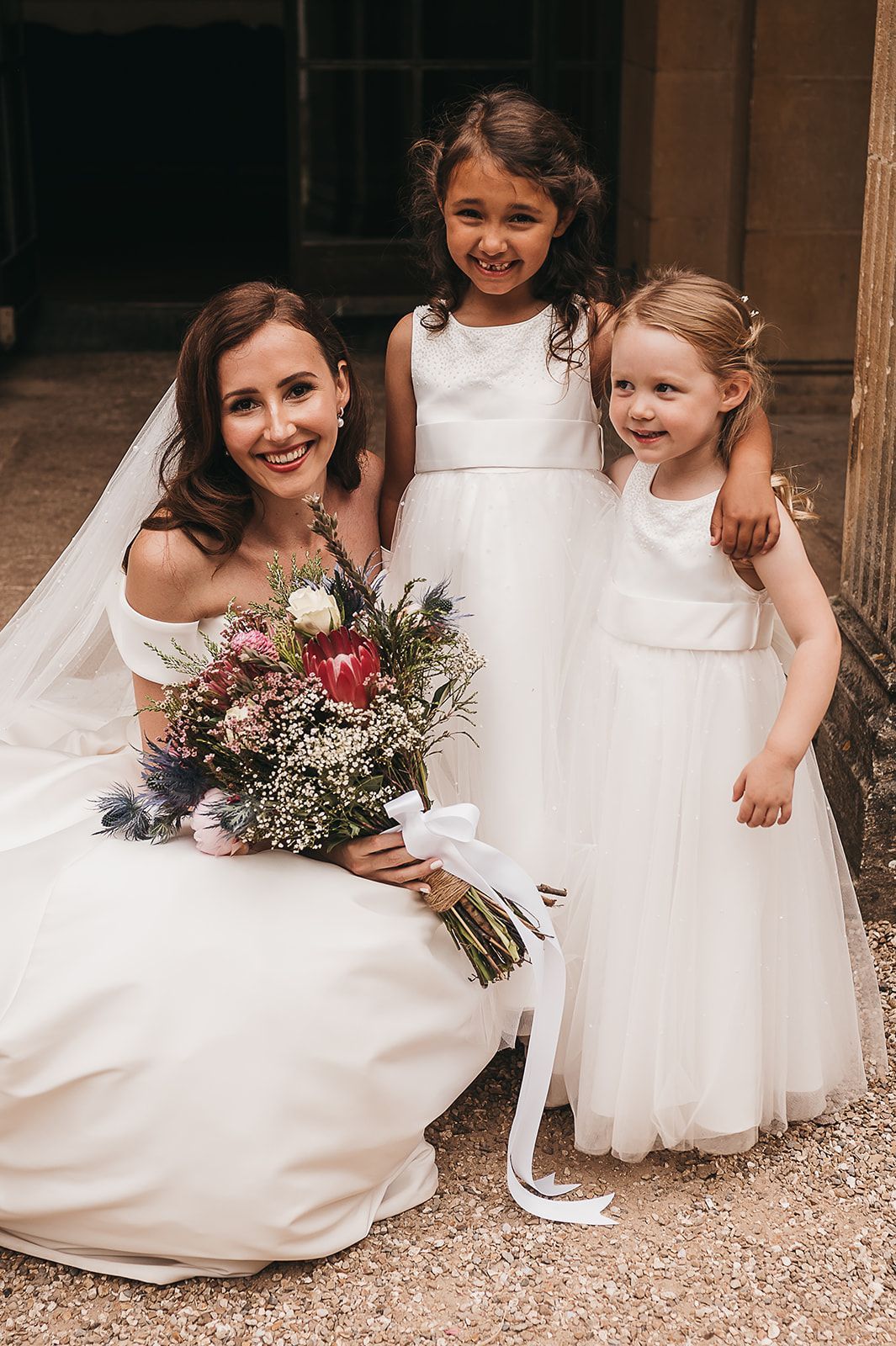 A bride and her two flower girls are posing for a picture.