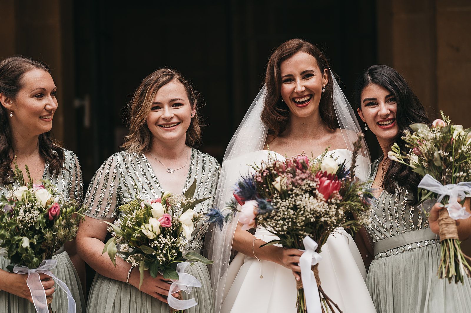 A bride and her bridesmaids are standing next to each other holding bouquets of flowers.