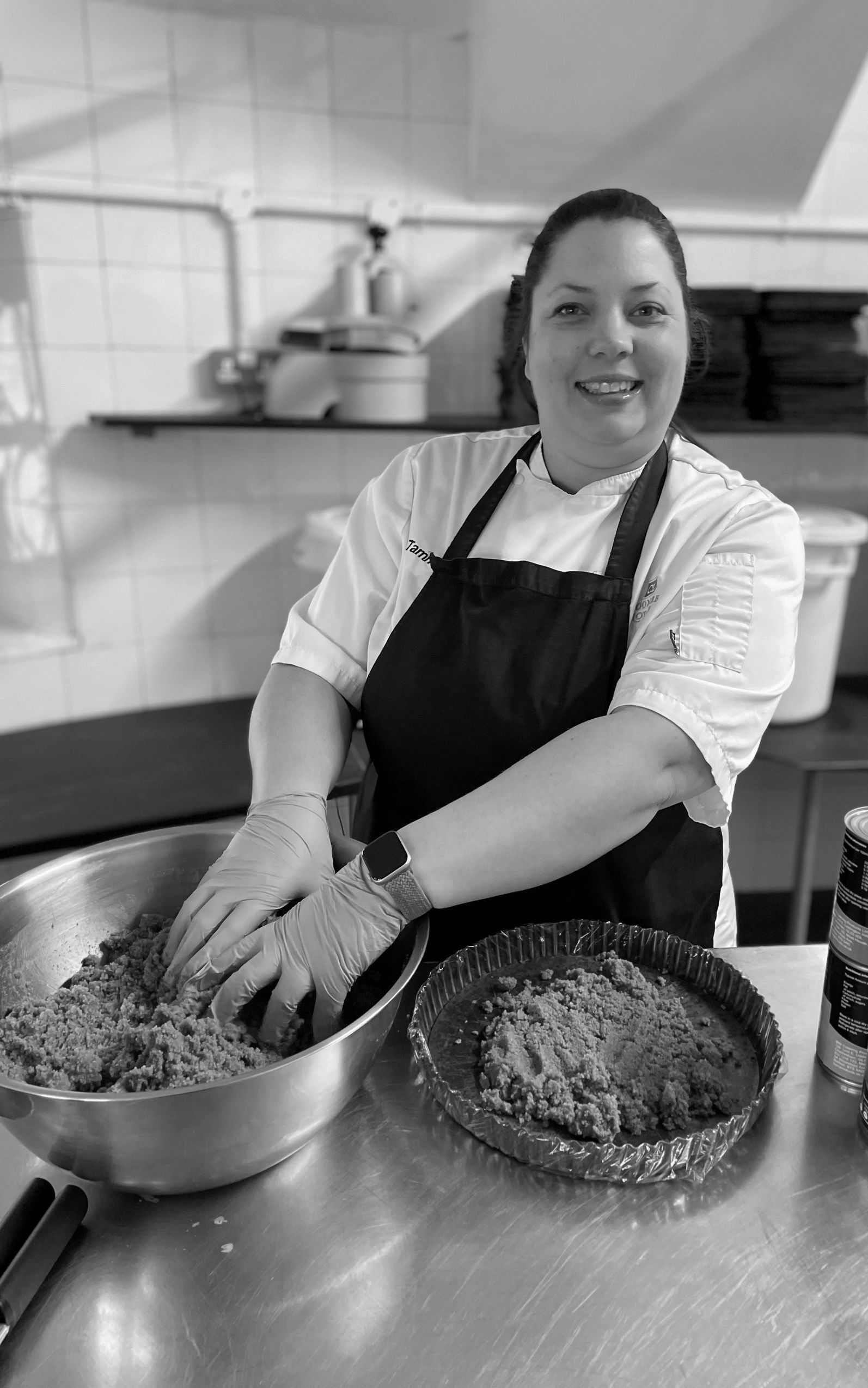 A black and white photo of a woman in an apron preparing food in a kitchen.