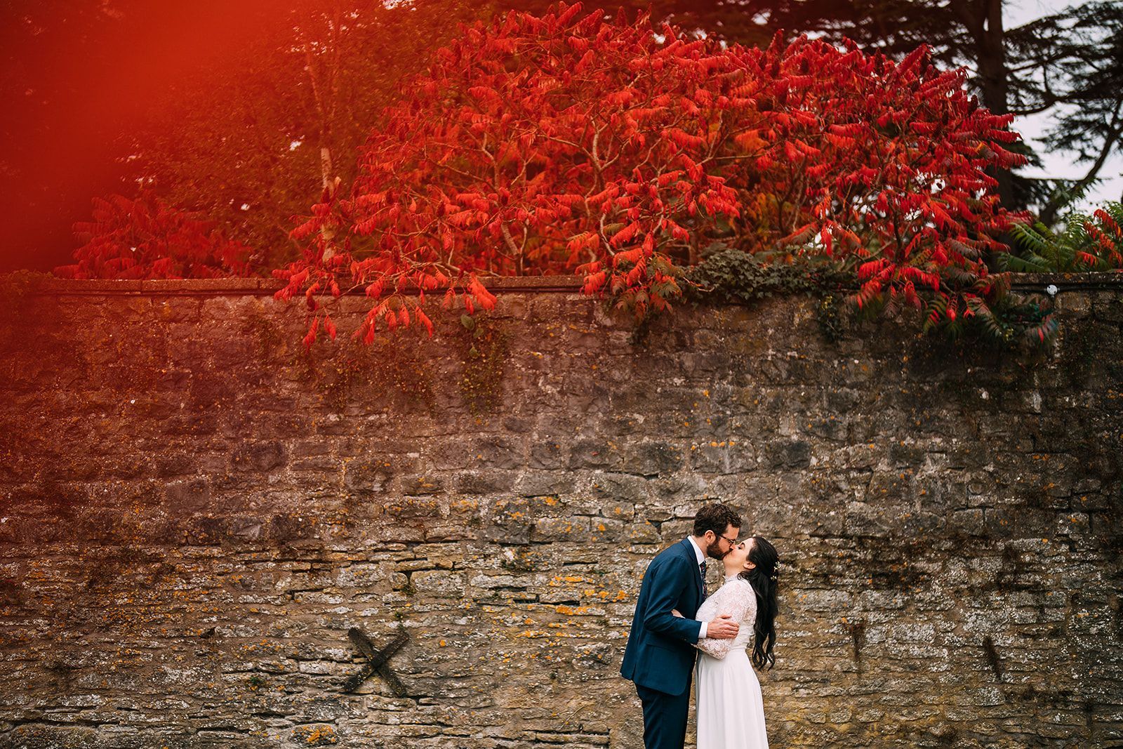 A bride and groom are kissing in front of a brick wall.