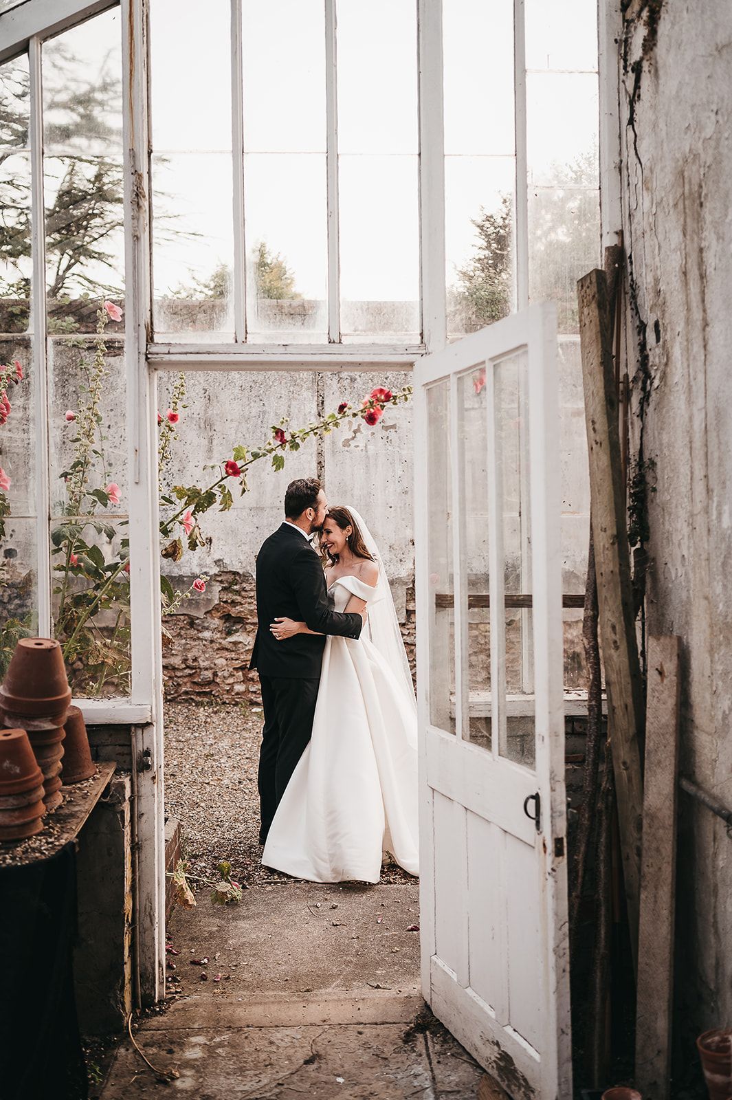 A bride and groom are hugging in a greenhouse.