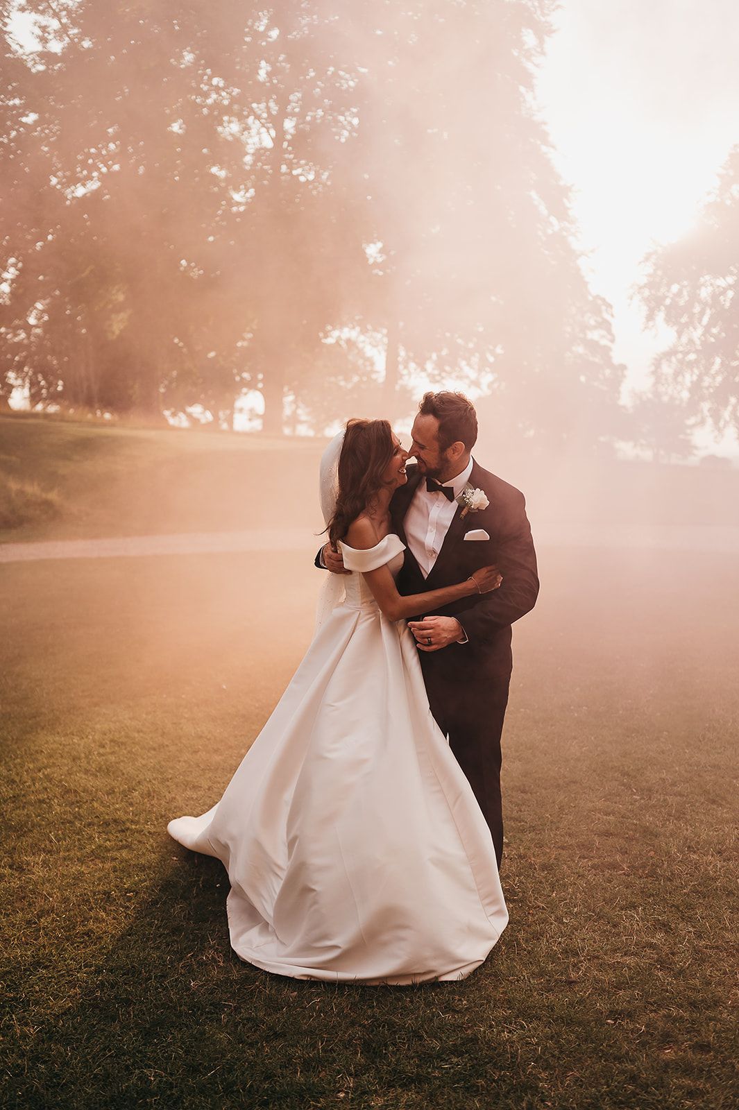 A bride and groom are kissing in a field surrounded by smoke.