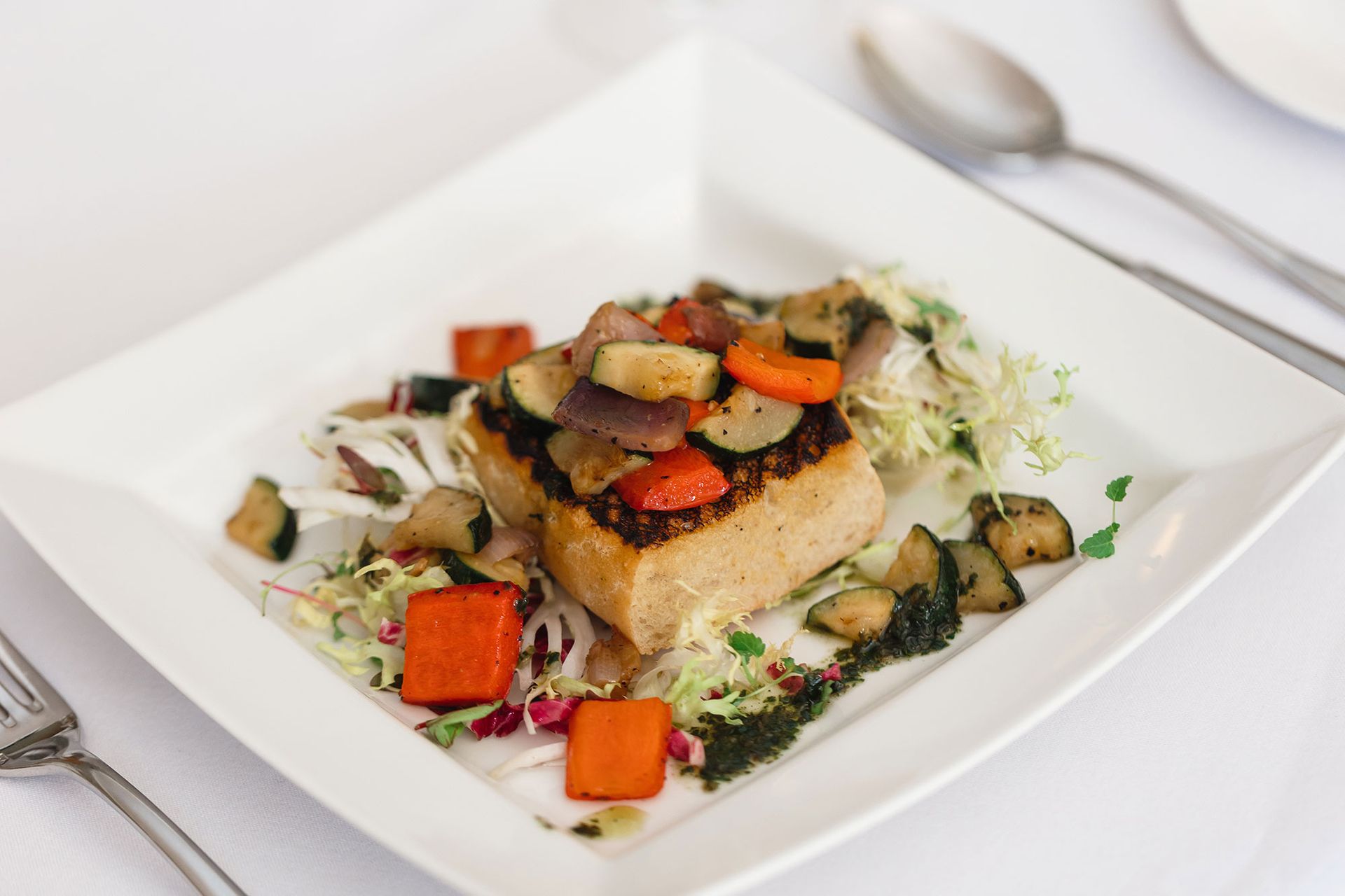 A white plate topped with a piece of meat and vegetables on a table.