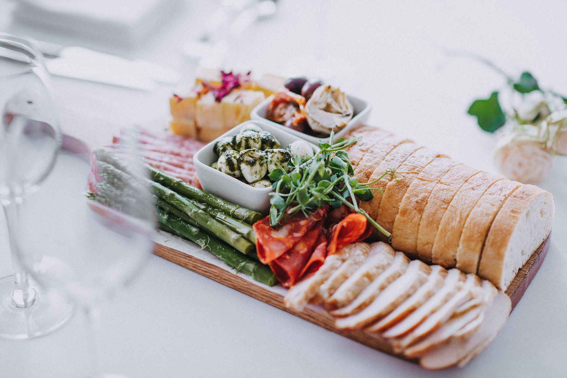 A wooden cutting board topped with sliced bread , vegetables and meat.