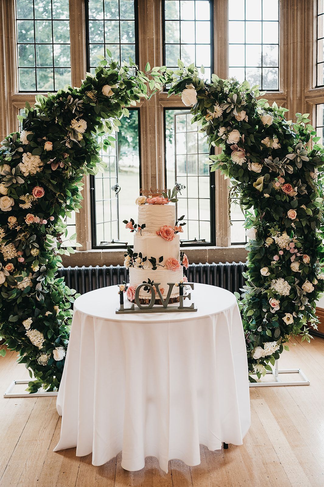 A wedding cake is sitting on a table in front of a floral arch.