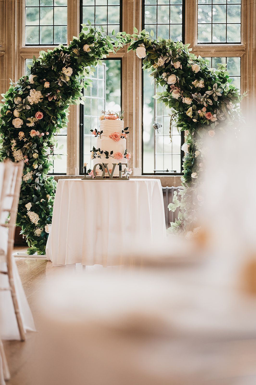 A wedding cake is sitting on a table under a floral arch.