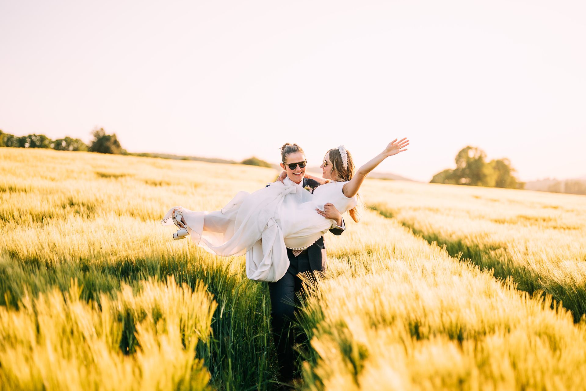 A man is carrying a bride in his arms in a field.