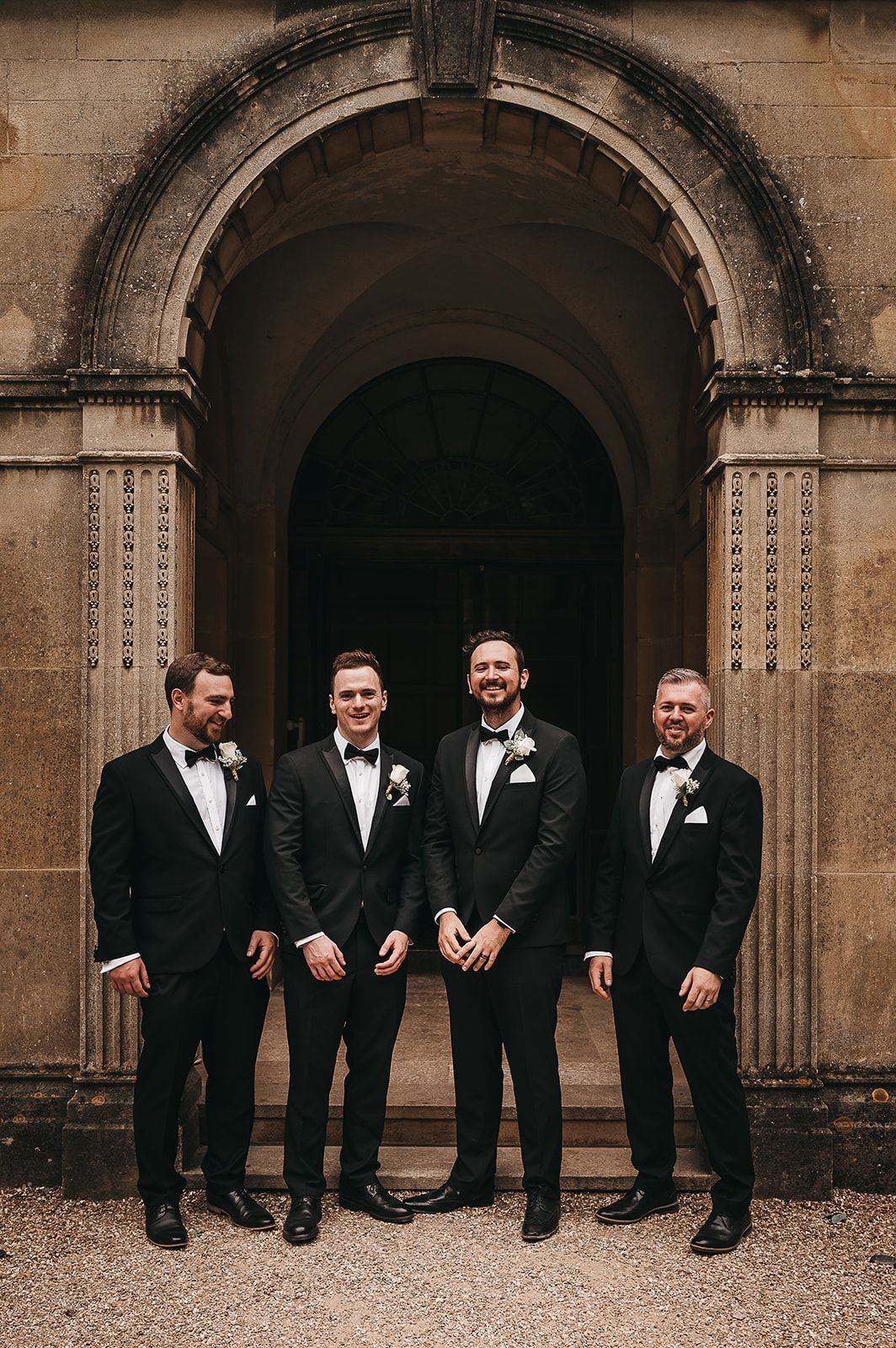 A group of men in tuxedos and bow ties are standing in front of a building.