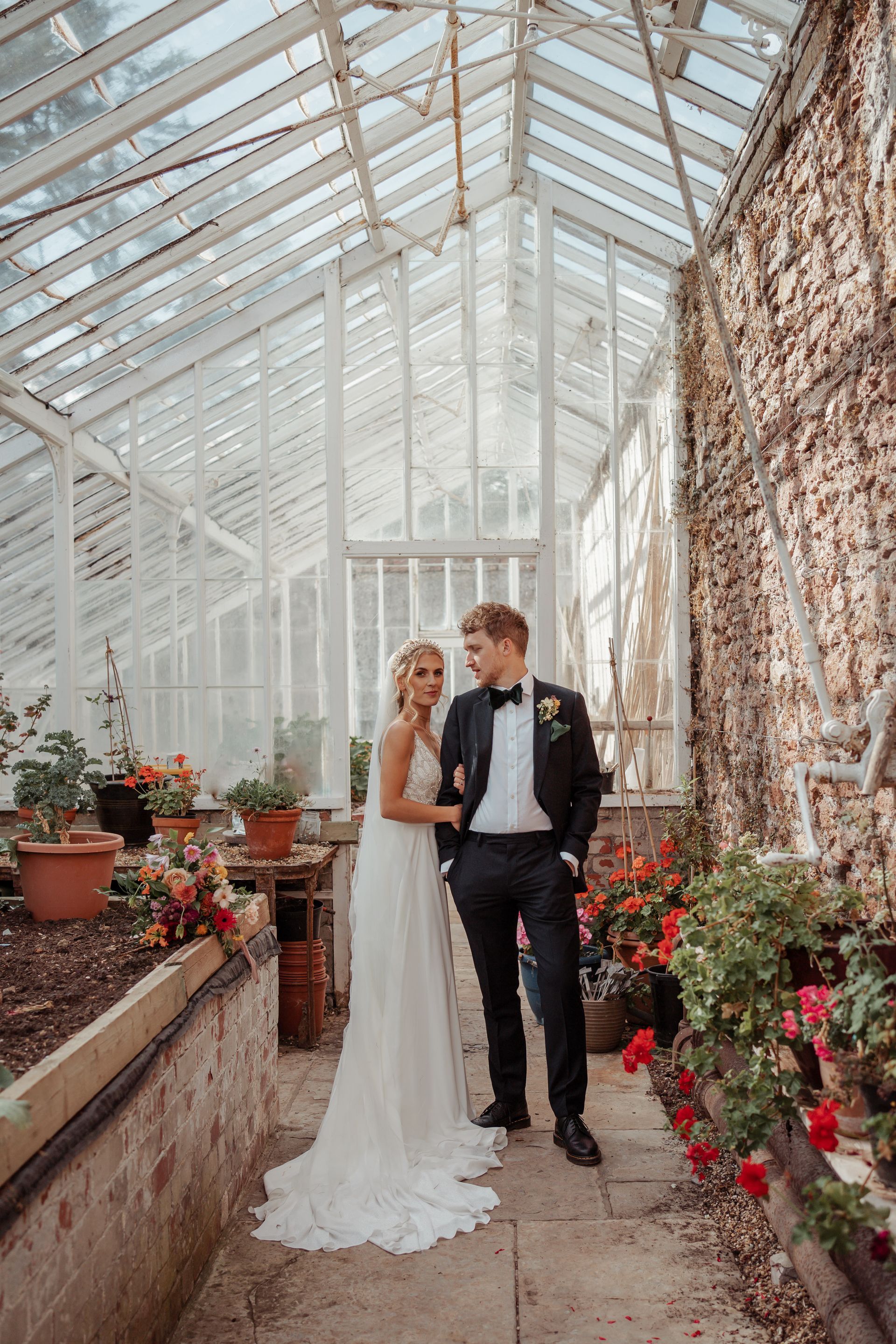A bride and groom are standing in a greenhouse.
