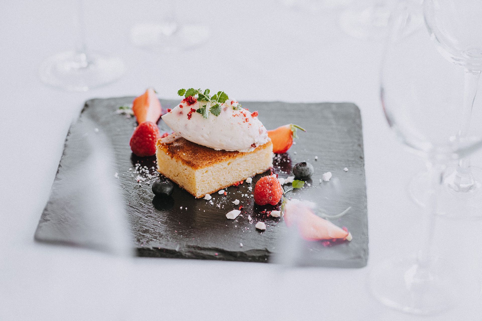 A piece of cake with whipped cream and strawberries on a black plate.