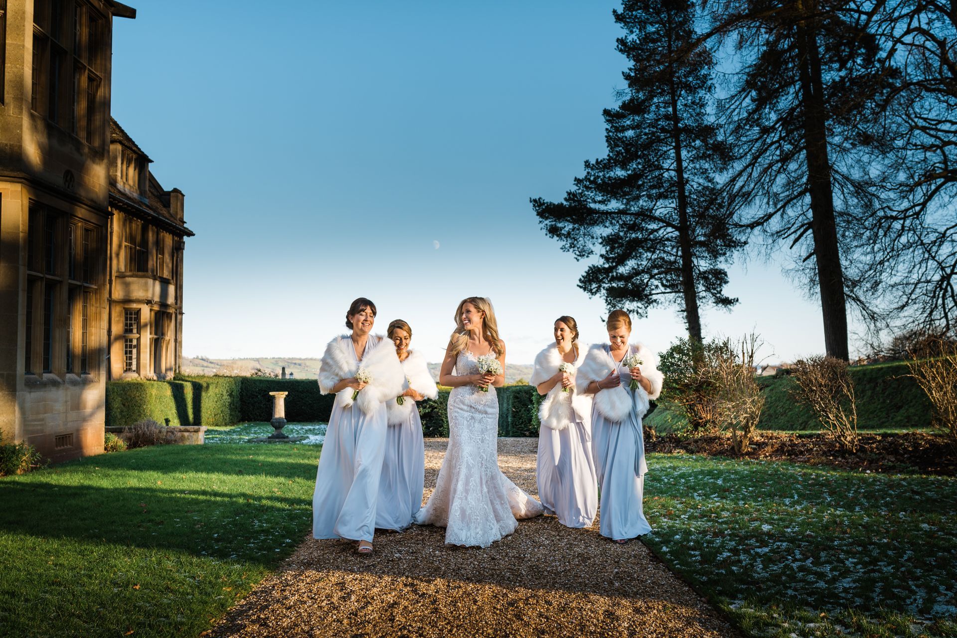 A bride and her bridesmaids are walking down a path in front of a building.