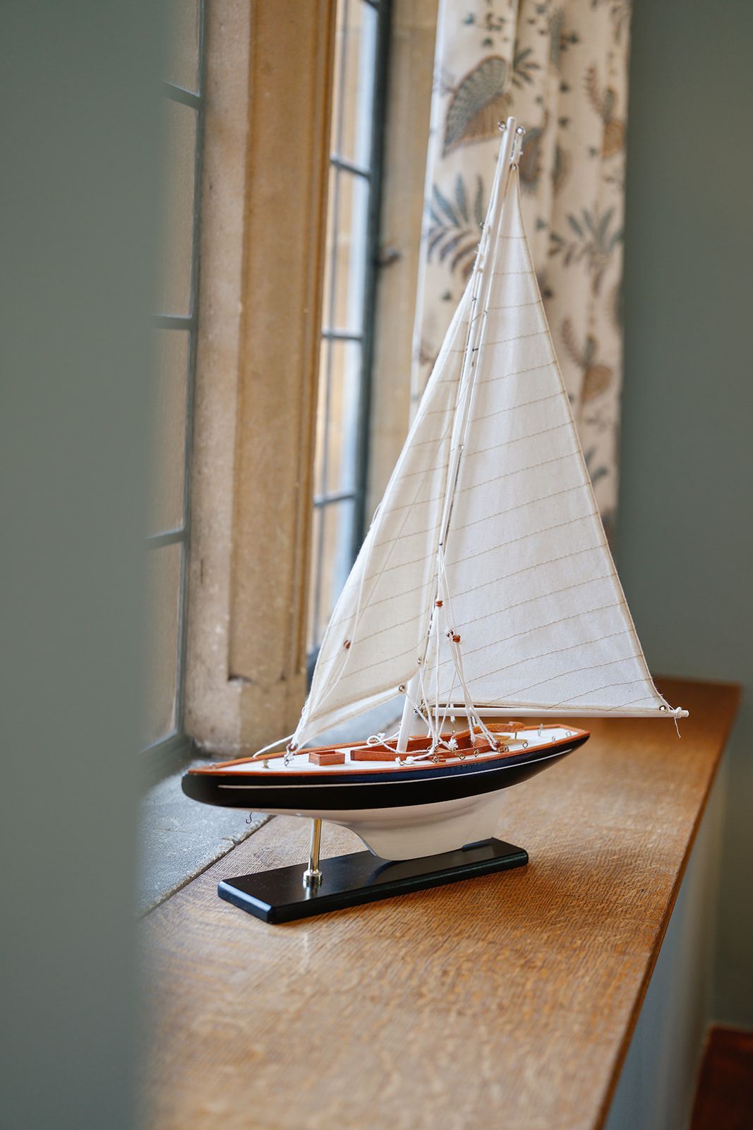 A model sailboat is sitting on a window sill.