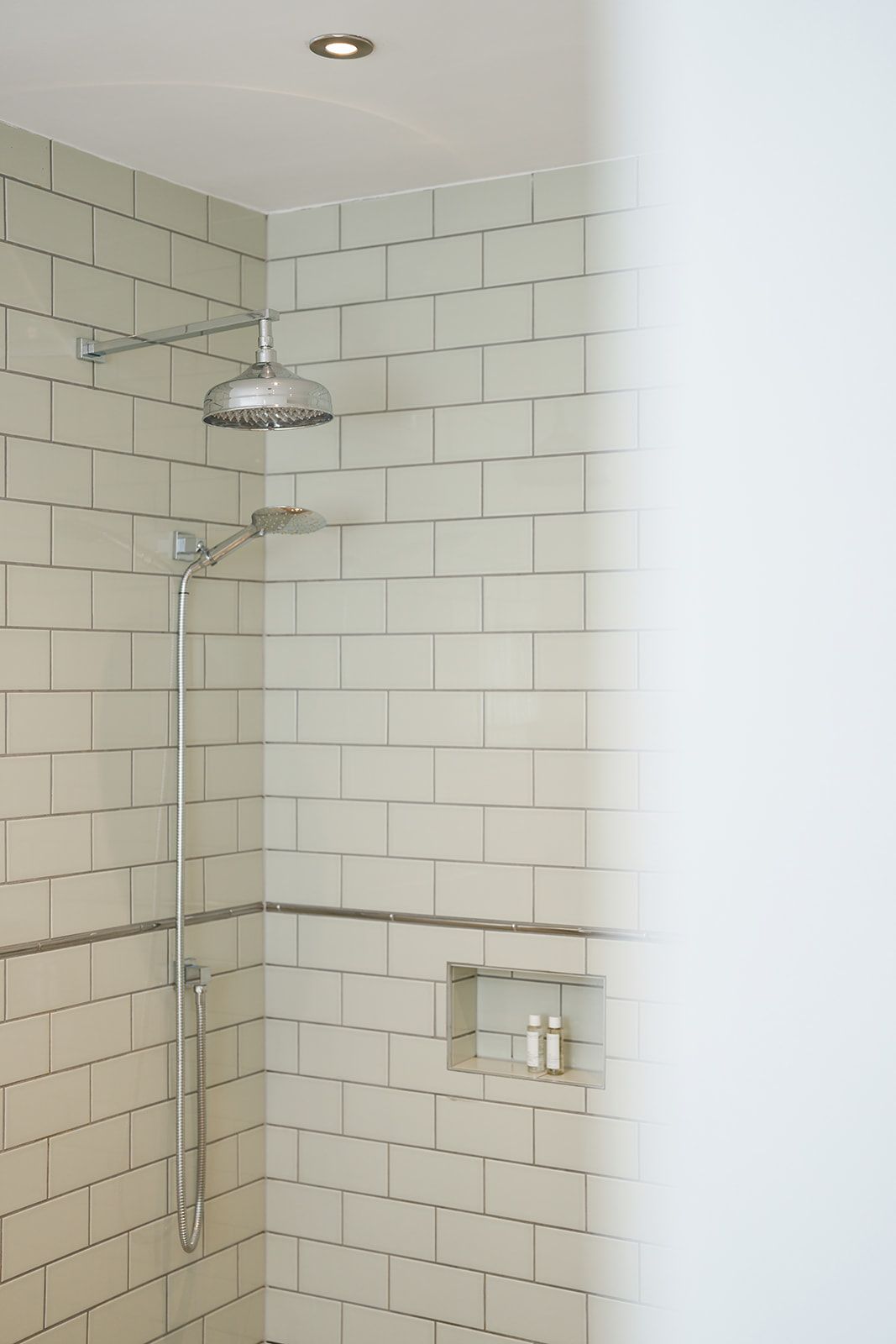 A bathroom with white tiles and a shower head.