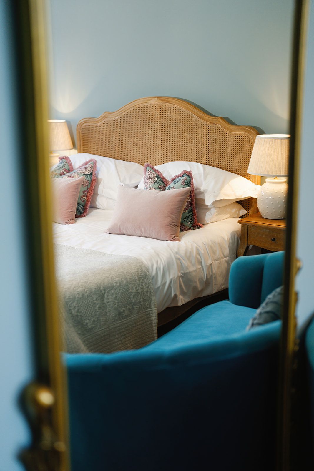 A bedroom with a bed , chair , lamp and mirror.