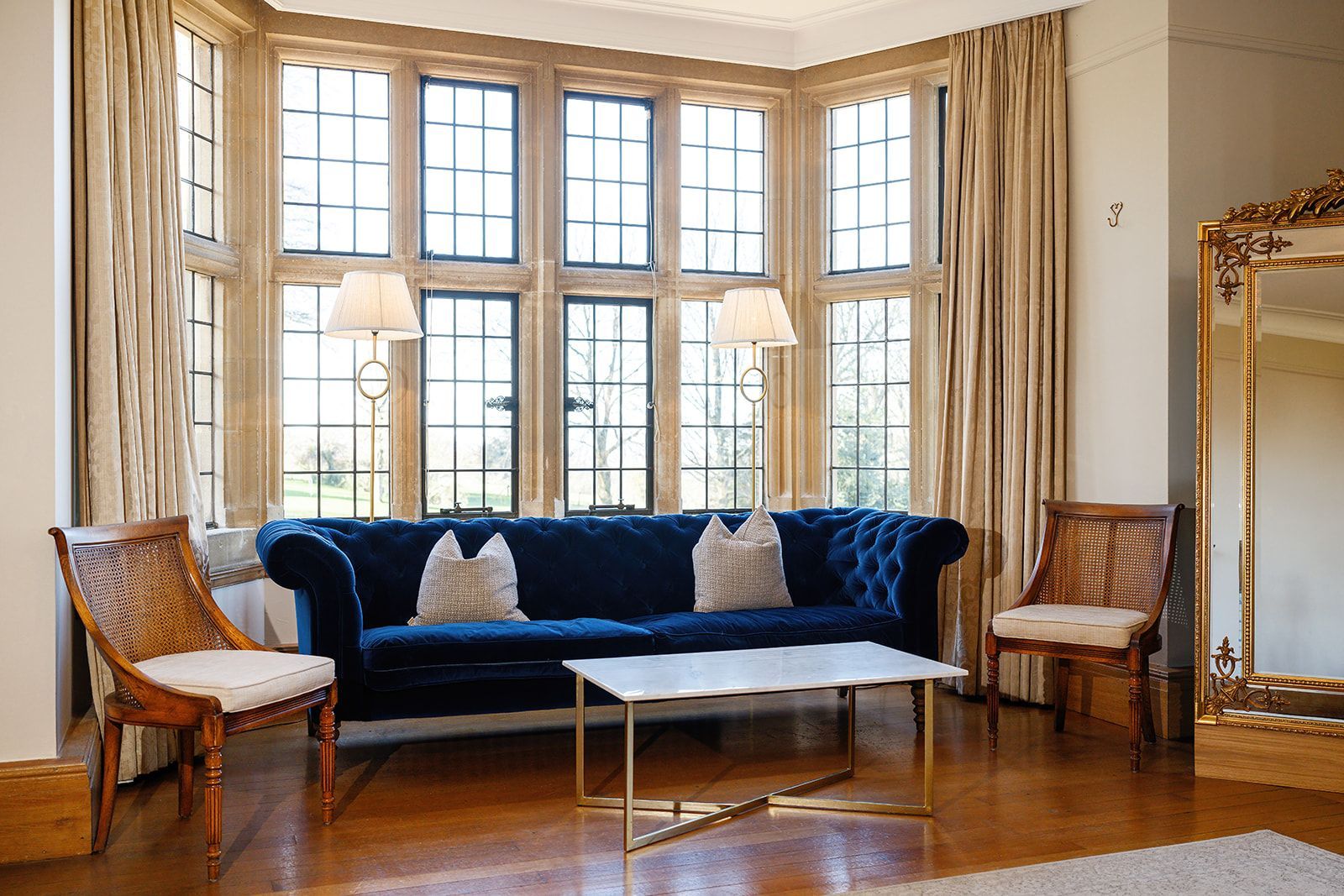 A living room with a blue couch , two chairs , a coffee table and a large mirror.