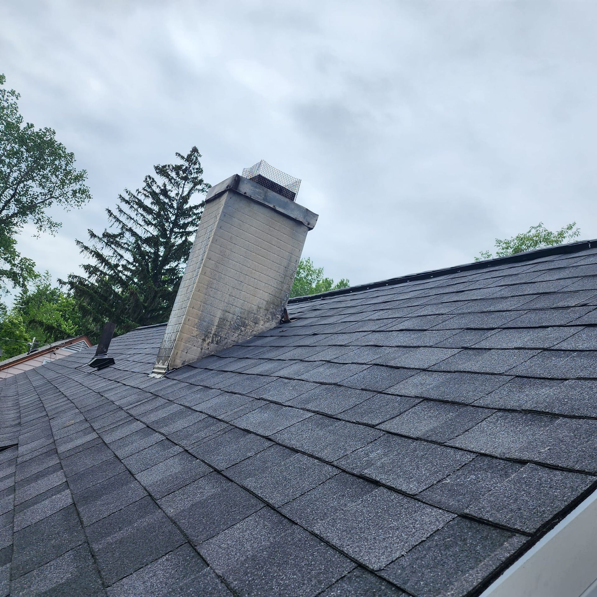 A roof with a chimney on top of it and trees in the background.