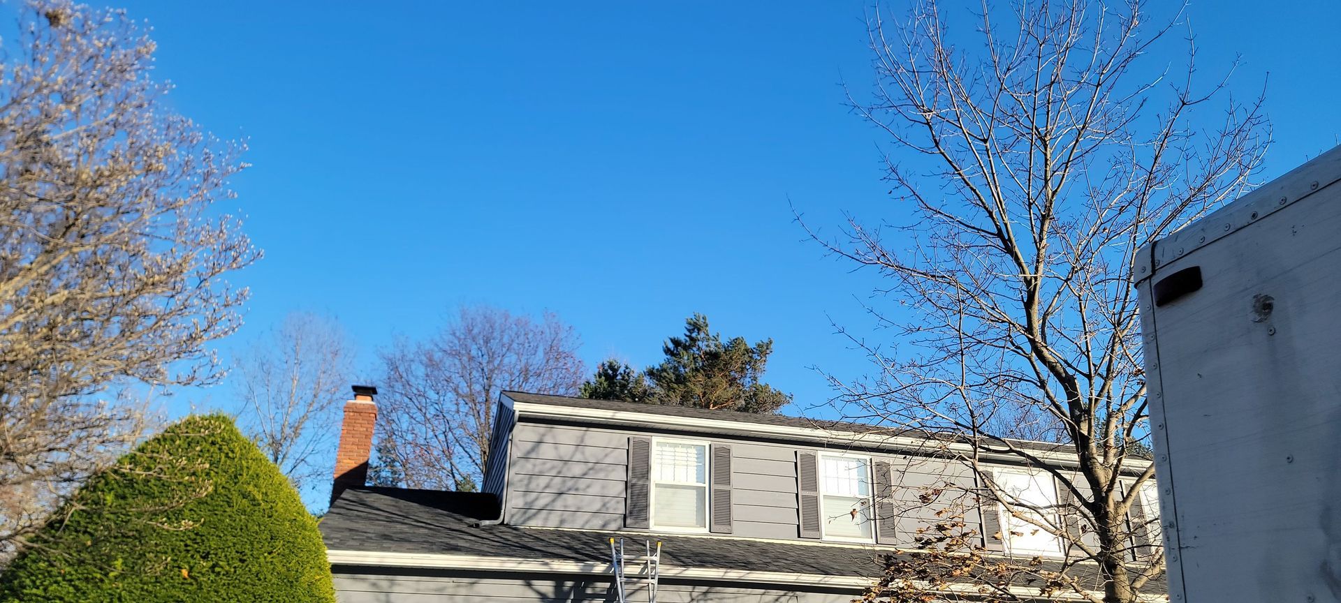 A house with a chimney on the roof is surrounded by trees on a sunny day.