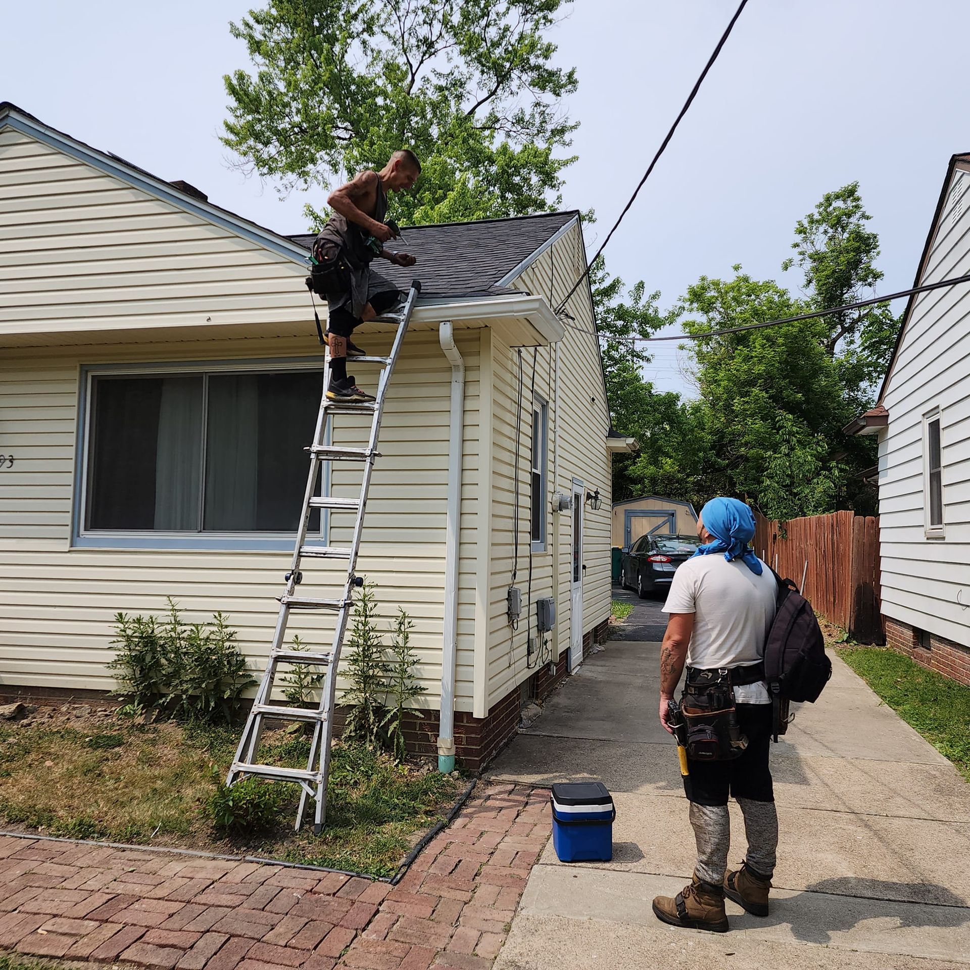 A man on a ladder is working on the roof of a house