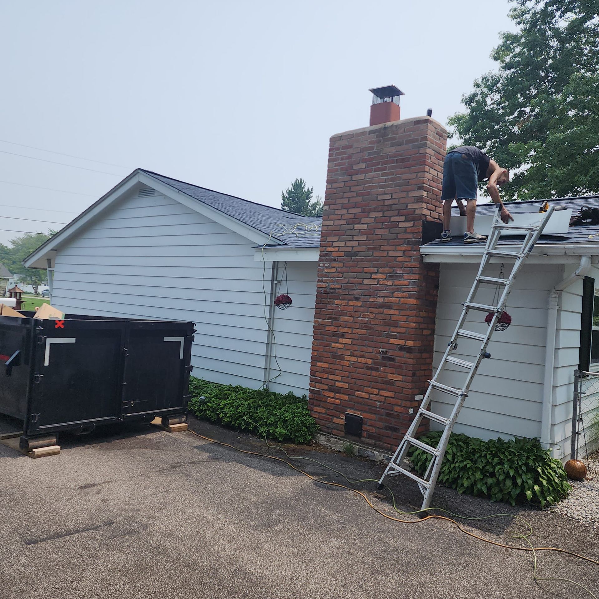 A man on a ladder is working on the roof of a house.