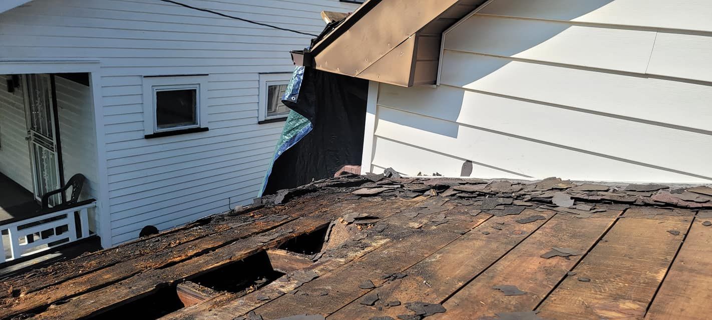 A roof with a hole in it and a white house in the background.