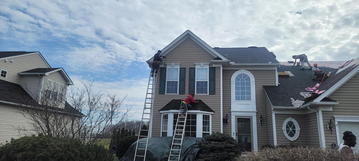 A man on a ladder is working on the roof of a house.