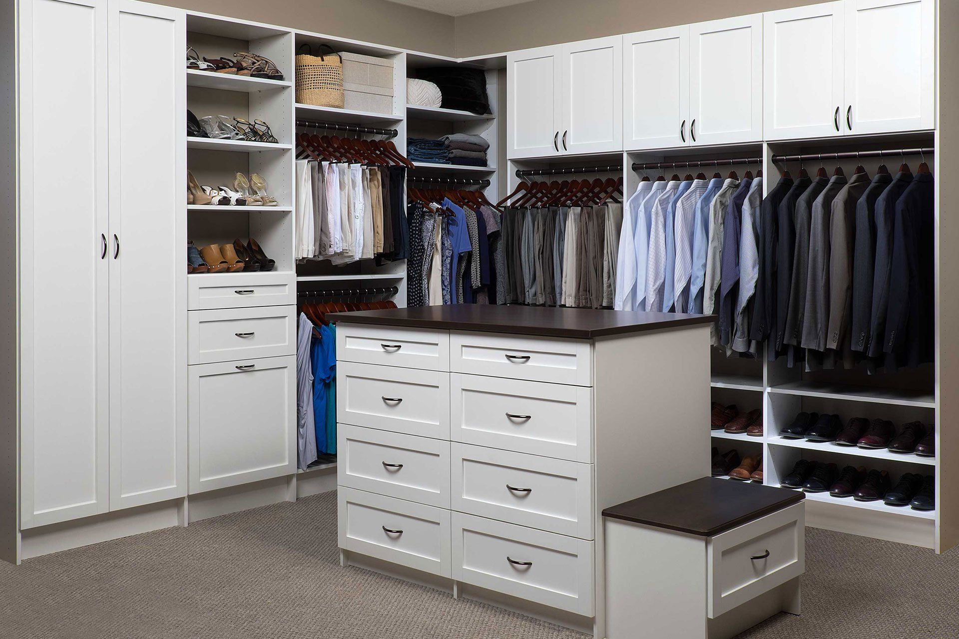 White walk-in closet with central island and bench. Clothes hanging, shoes on shelves.